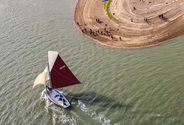 Oyster smack Peace sails past East Mersea Stone on the River Blackwater in Essex, watching by a crowd of spectators