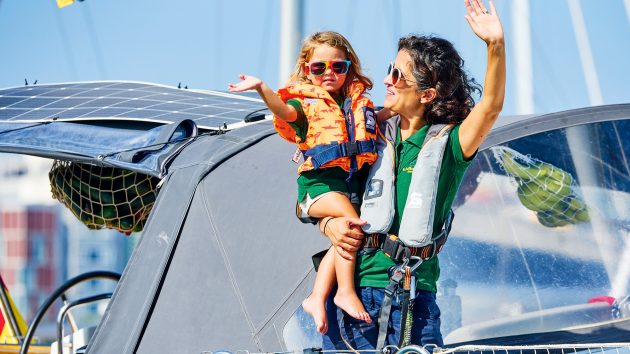 Mashal and Lonneke waving to the camera aboard their yacht. Both wear life jackets and sunglasses